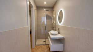Un baño moderno con ducha envuelta en vidrio, un lavamanos blanco y dos espejos ovalados con luz.