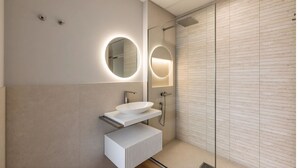 Un baño moderno con un lavamanos blanco, un espejo redondo con iluminación y una zona de ducha.