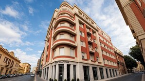 Un edificio de varios pisos con fachada curva, una entrada destacada y cielo despejado.