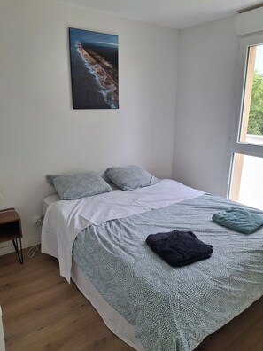 Un dormitorio con cama, almohadas, una colcha, una mesita de noche y un cuadro colgado en la pared.
