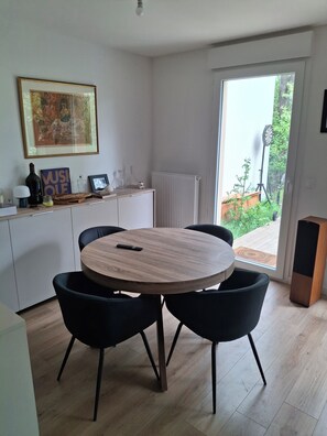 Un comedor con una mesa redonda de madera, sillas negras, un armario blanco, un cuadro enmarcado y un radiador.