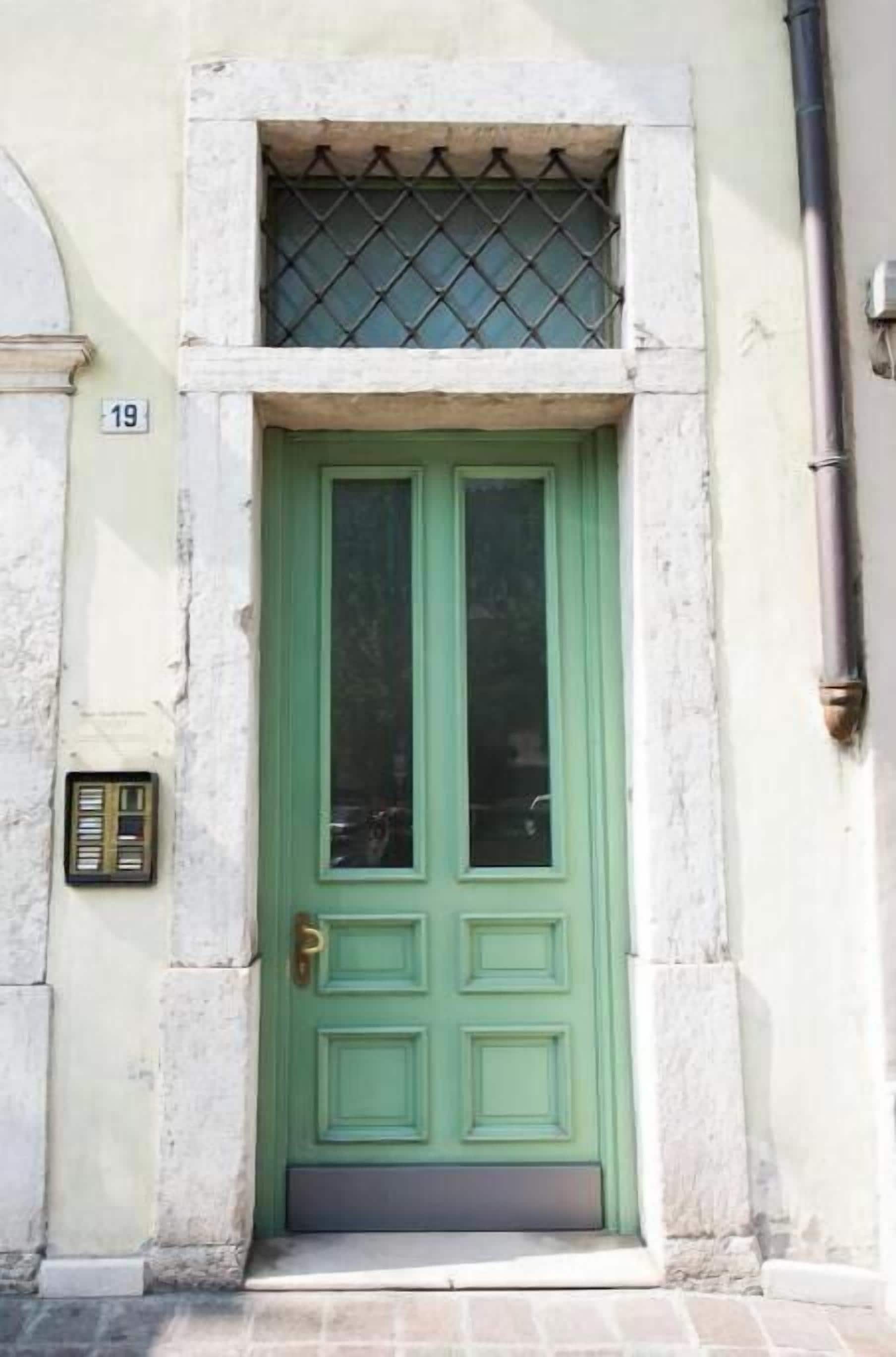 A green door with a small window above it, a number '19' on the wall, and a metal grate on the window.