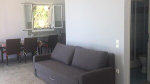 Een zithoek met een bank, stoelen, een eettafel en een keukenhoek met een raam.