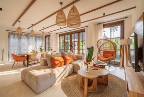 Un salon moderne avec un canapé d’angle, un coin repas et de grandes fenêtres.