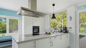 Een moderne keuken met witte kastjes, een inbouwoven, een koffiezetapparaat en een groot raam met uitzicht op groen.