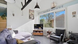 Een moderne woonkamer met een bank, een zwarte lederen fauteuil, een televisie en een open haard.