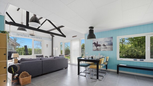 Een moderne woonkamer met een grijze bank, een eettafel met stoelen en een groot raam met uitzicht op groen.