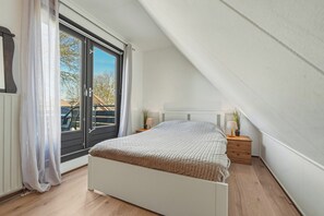 A bedroom with a bed, a nightstand, a lamp, a window with curtains, and a view of the outside. - Enjoy peace, space and comfort at Haringvliet 93 in Noordzeepark Ouddorp. This charming holiday home is located close to the beach and nature, making it ideal for families, friends and dog lovers. (Ouddorp)