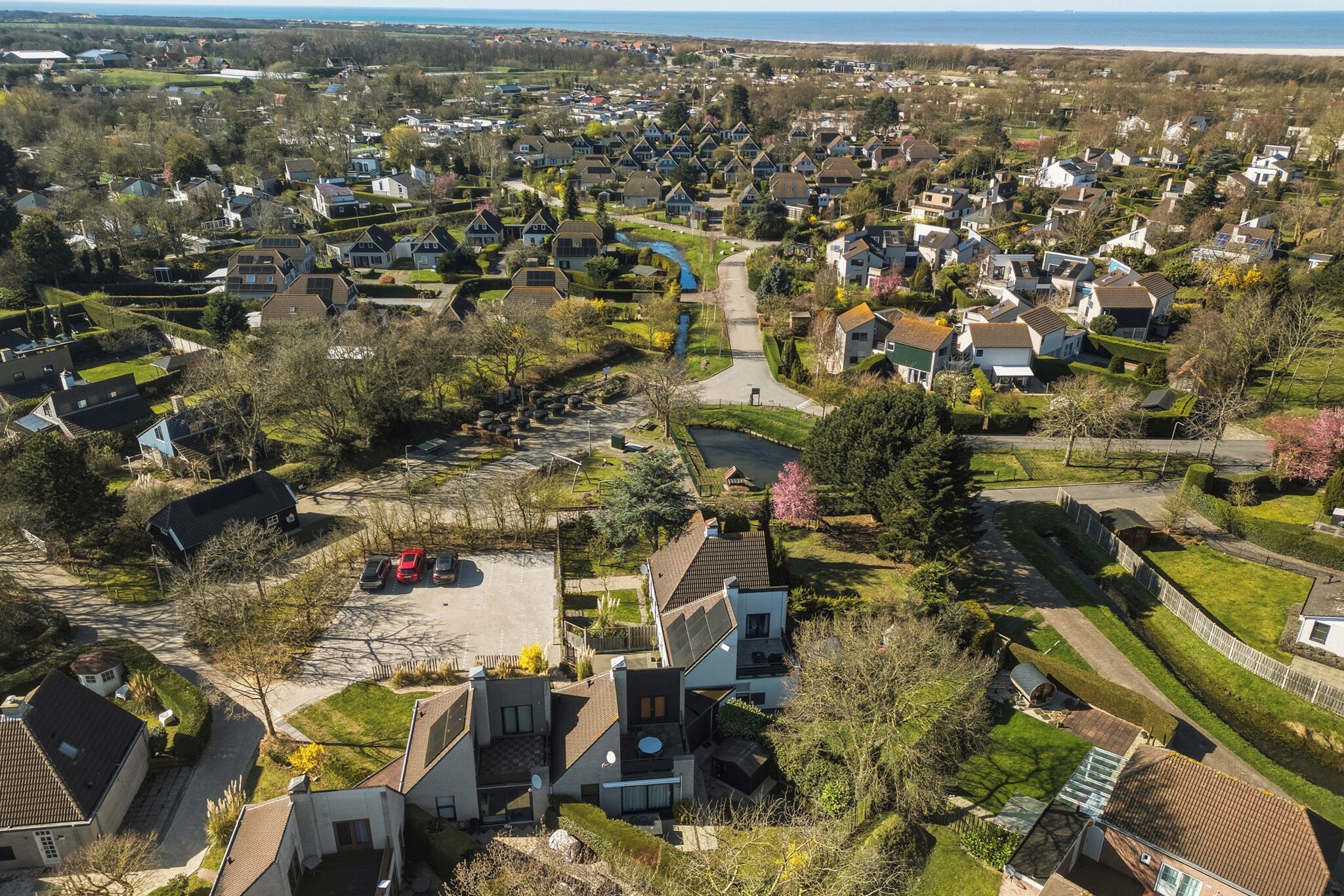 Vista aérea de una zona residencial con casas, un río y una playa al fondo.