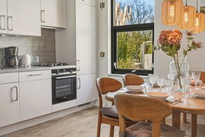 A modern kitchen with white cabinets, a stove, and a dining area with chairs and a table set for four. - Enjoy peace, space and comfort at Haringvliet 93 in Noordzeepark Ouddorp. This charming holiday home is located close to the beach and nature, making it ideal for families, friends and dog lovers. (Ouddorp)