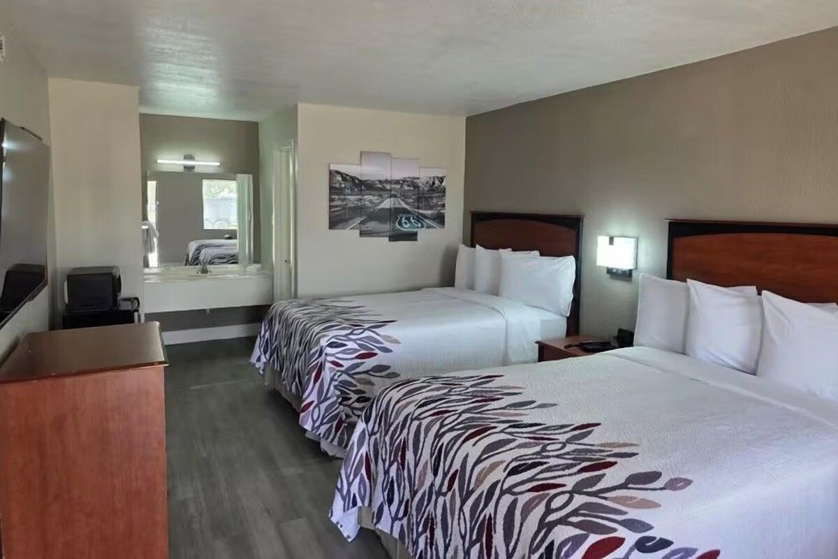 A hotel room with two beds, a desk, a chair, a mirror, and a painting on the wall.