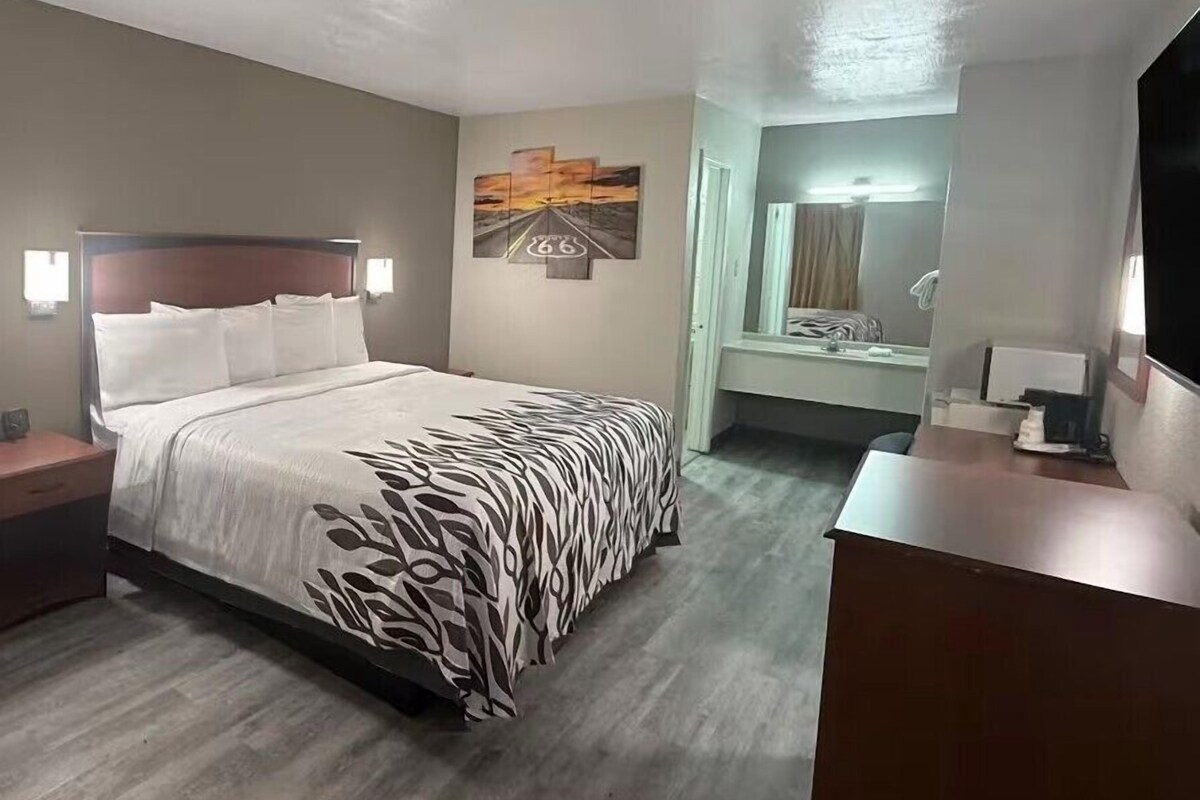 A hotel room with a bed, bedside tables, a desk, a mirror, and artwork on the walls.