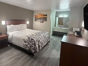 A hotel room with a bed, bedside tables, a desk, a mirror, and artwork on the walls.