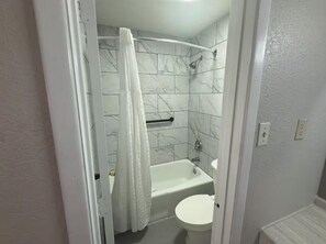 A bathroom with a bathtub, toilet, and shower curtain.
