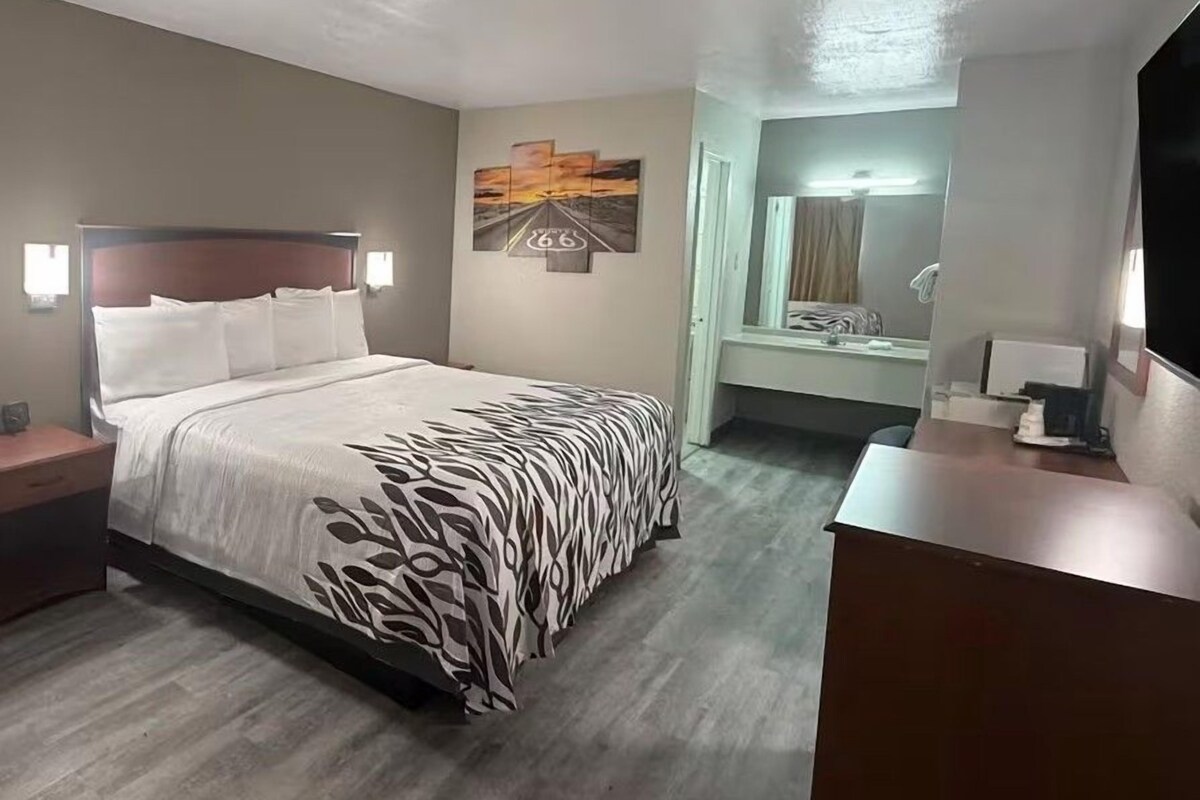 A hotel room with a bed, bedside tables, a desk, a mirror, and artwork on the walls.