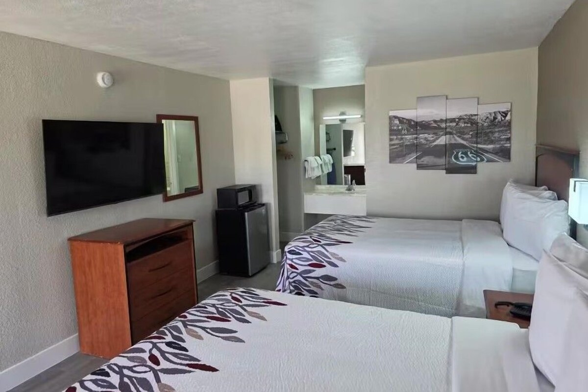 A hotel room with two beds, a television, a desk, and a mirror.