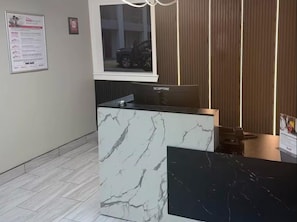 A reception desk with a marble design, a computer monitor, and a framed picture on the wall.