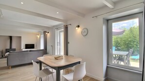 A modern living room with a dining area, a sofa, a TV, and a large window with a view of greenery. - Holiday Home 'Gite Baie' with Private Terrace, Private Garden and Wi-Fi (Telgruc-sur-Mer)
