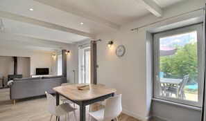 Ein modernes Wohnzimmer mit Essbereich, einer Couch, einem Fernseher und einem großen Fenster mit Blick auf Grünflächen.