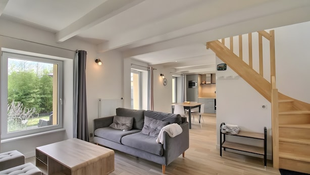 A modern living room with a grey sofa, wooden coffee table, and a staircase leading to a kitchen area. - Holiday Home 'Gite Baie' with Private Terrace, Private Garden and Wi-Fi (Telgruc-sur-Mer)