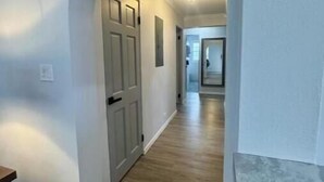 A hallway with a wooden floor, white walls, and a door with a light fixture above it. - Peaceful Bermuda Retreat Near Beaches & Royal Naval Dockyard (Sandys Parish)