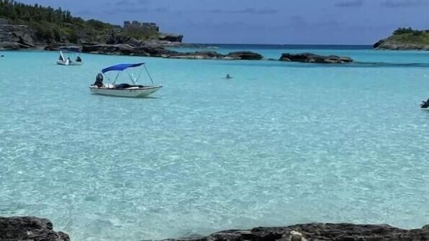 A coastal scene with clear turquoise water, a boat with a blue canopy, and rocky terrain. - Peaceful Bermuda Retreat Near Beaches & Royal Naval Dockyard (Sandys Parish)