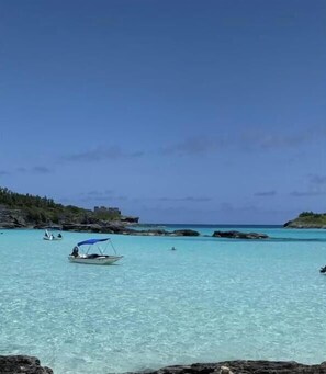 Eine Küstenlandschaft mit klarem türkisblauem Wasser, einem Boot mit blauem Verdeck und felsigem Gelände.
