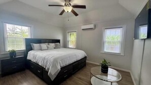 A bedroom with a bed, a ceiling fan, a round glass table, and two windows. - Peaceful Bermuda Retreat Near Beaches & Royal Naval Dockyard (Sandys Parish)