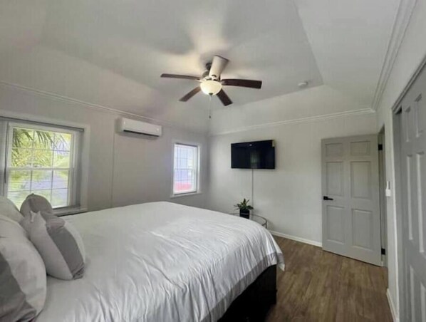 Ein Schlafzimmer mit einem Bett, Deckenventilator, Fernseher und einer Tür.