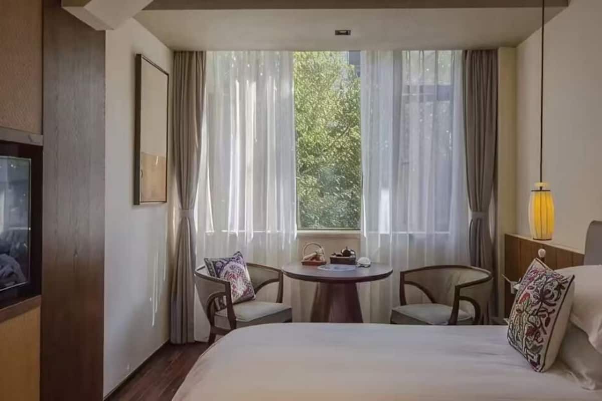 Ein Hotelzimmer mit Bett, Fernseher, Esstisch mit Stühlen und einem Fenster mit Vorhängen.