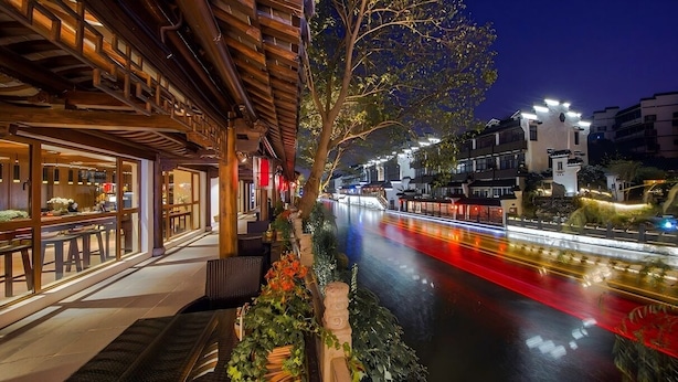 A riverside restaurant with outdoor seating, a wooden structure, and a view of the river. - Yeboqinhuai SSAW BOUTIQUE Hotel(Jinling Calligraphy and Painting Academy) (Nanjing)