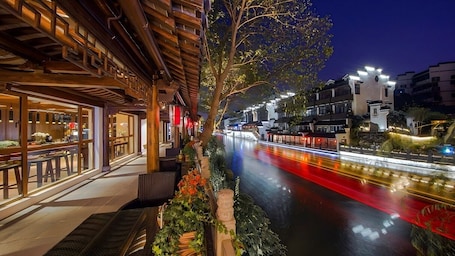 A riverside restaurant with outdoor seating, a wooden structure, and a view of the river.. Yeboqinhuai SSAW BOUTIQUE Hotel Qinhuai