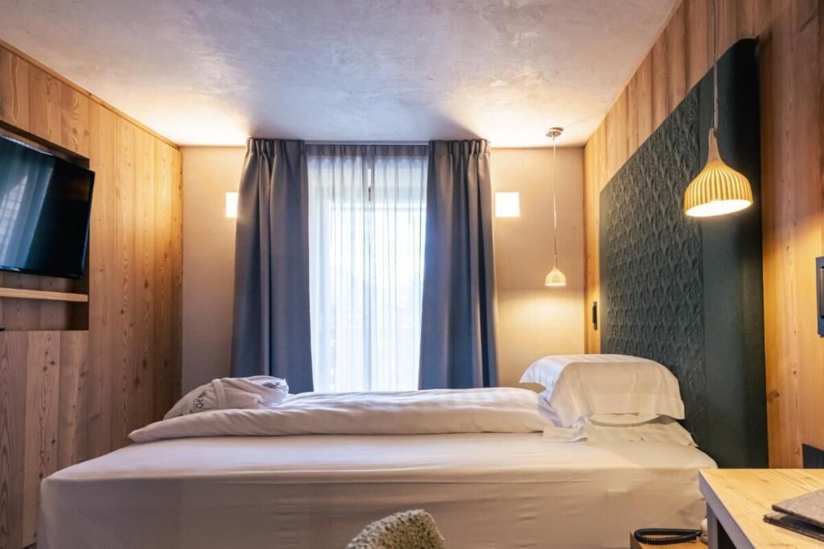 Une chambre d’hôtel avec un lit, des rideaux, un téléviseur et un luminaire fixé au mur.