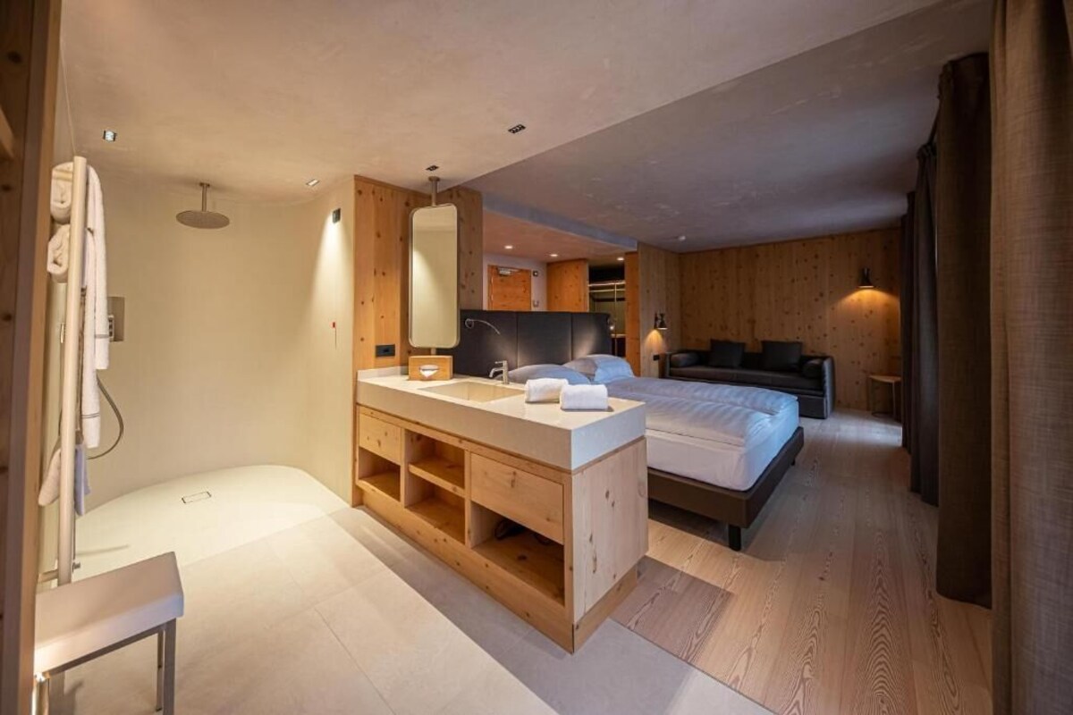 Une chambre d’hôtel moderne avec une coiffeuse en bois, un grand lit et un coin salon séparé.