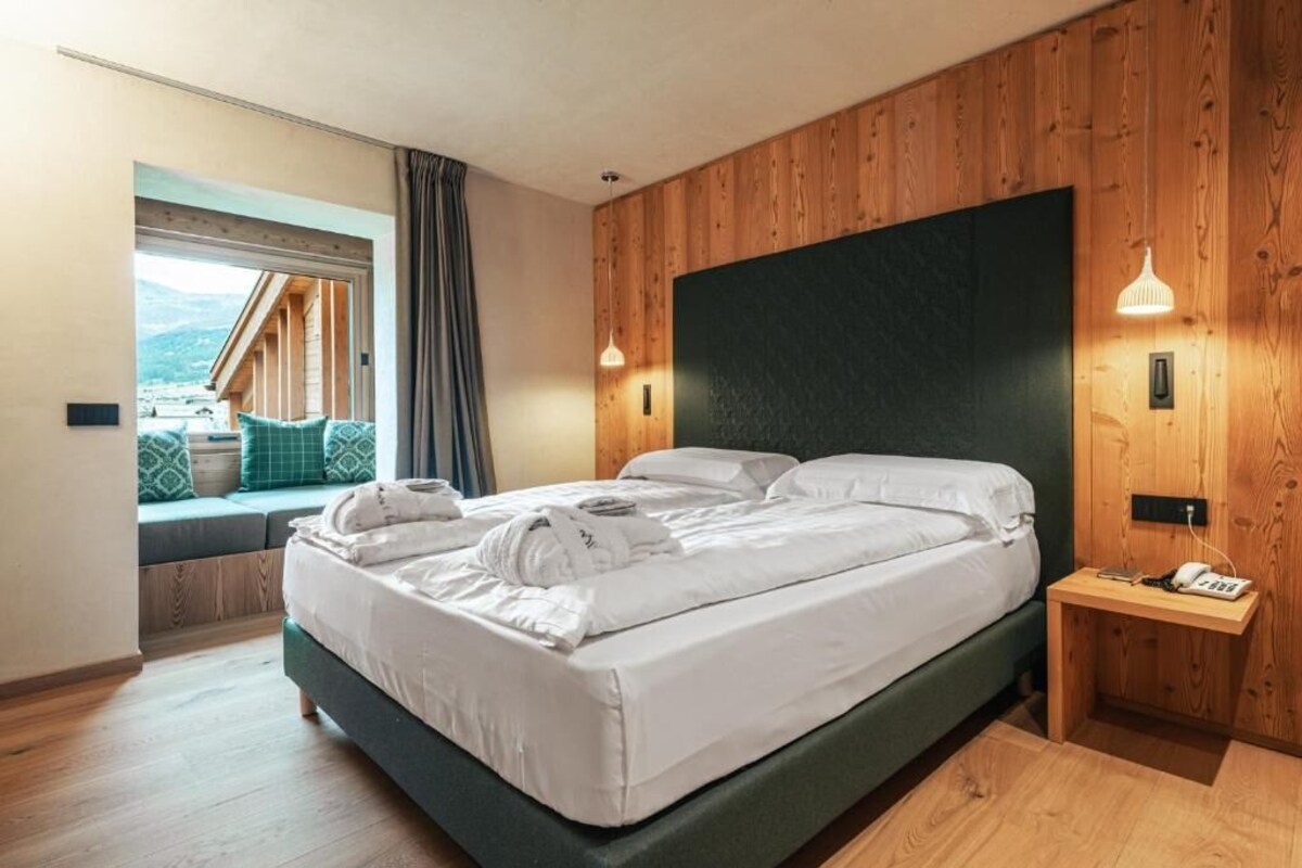 Une chambre d’hôtel moderne avec un grand lit, des murs recouverts de panneaux de bois, une petite table de chevet avec un téléphone et une fenêtre donnant sur l’extérieur.