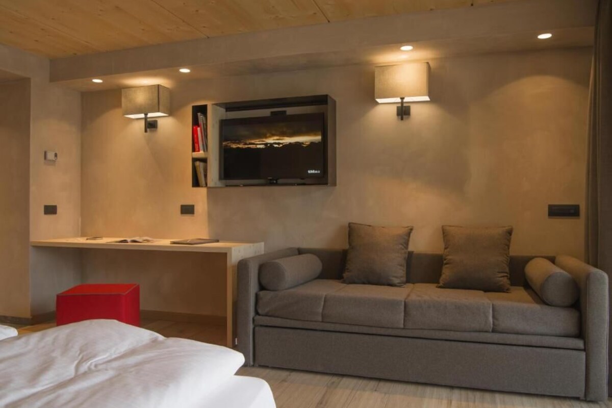 Une chambre d’hôtel moderne équipée d’un canapé, d’un bureau, d’une télévision à écran plat et de deux lampes fixées au mur.