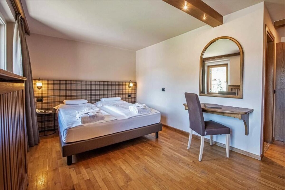 Une chambre à coucher comprenant un lit, un bureau, une chaise, un miroir et une table de chevet.