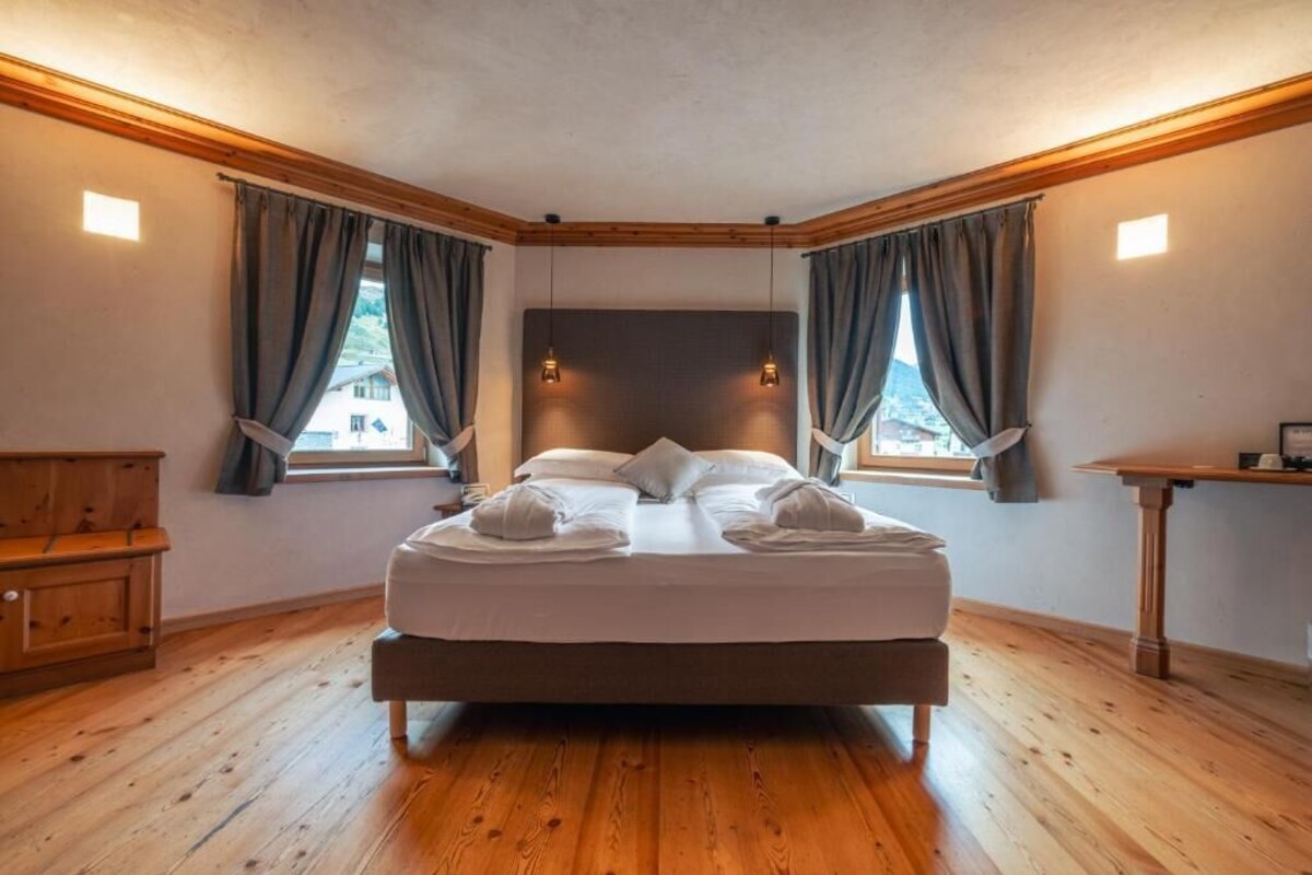 Une chambre à coucher avec un lit, un plancher en bois, des rideaux et une petite table.
