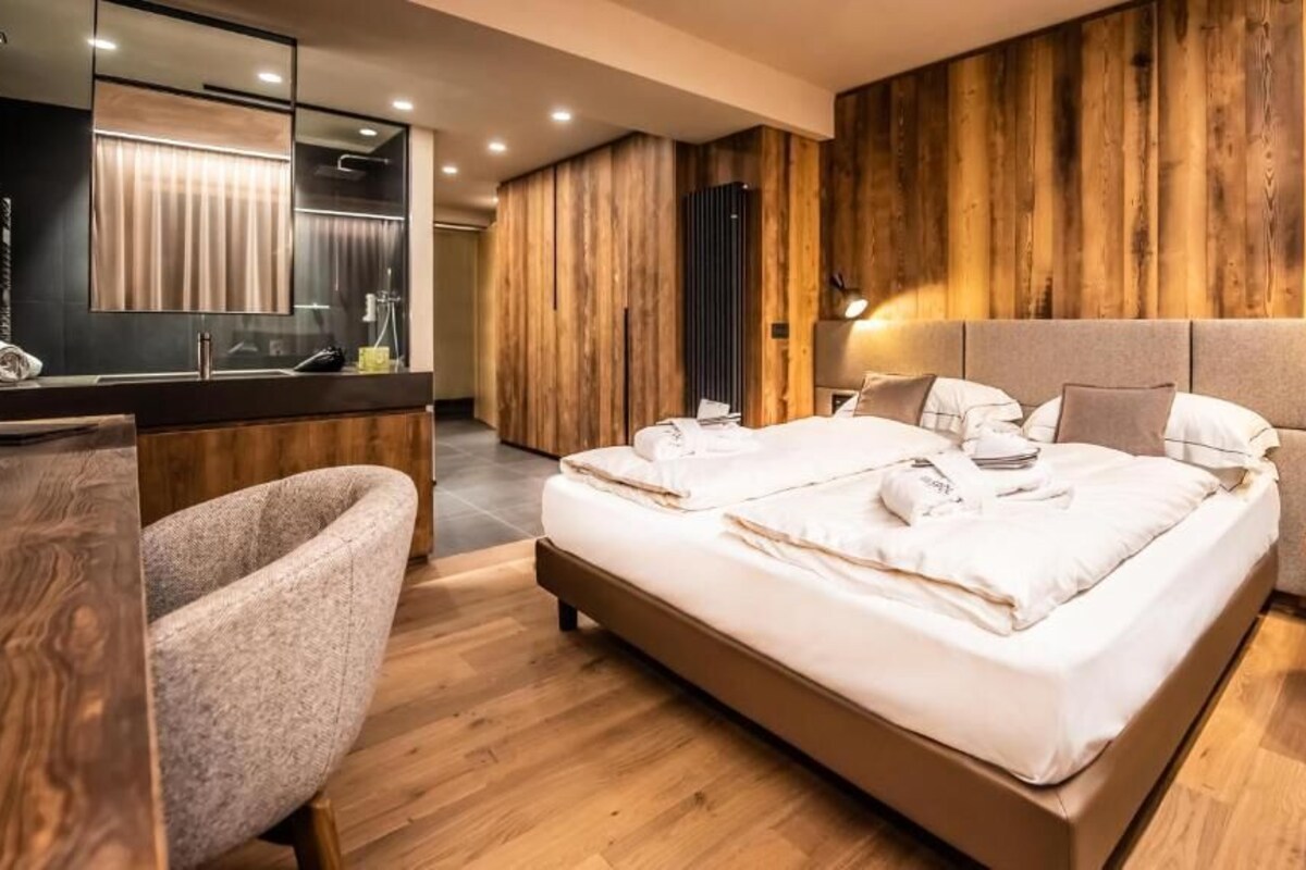Une chambre à coucher moderne avec un grand lit, une tête de lit en bois, une table de chevet et une chaise.
