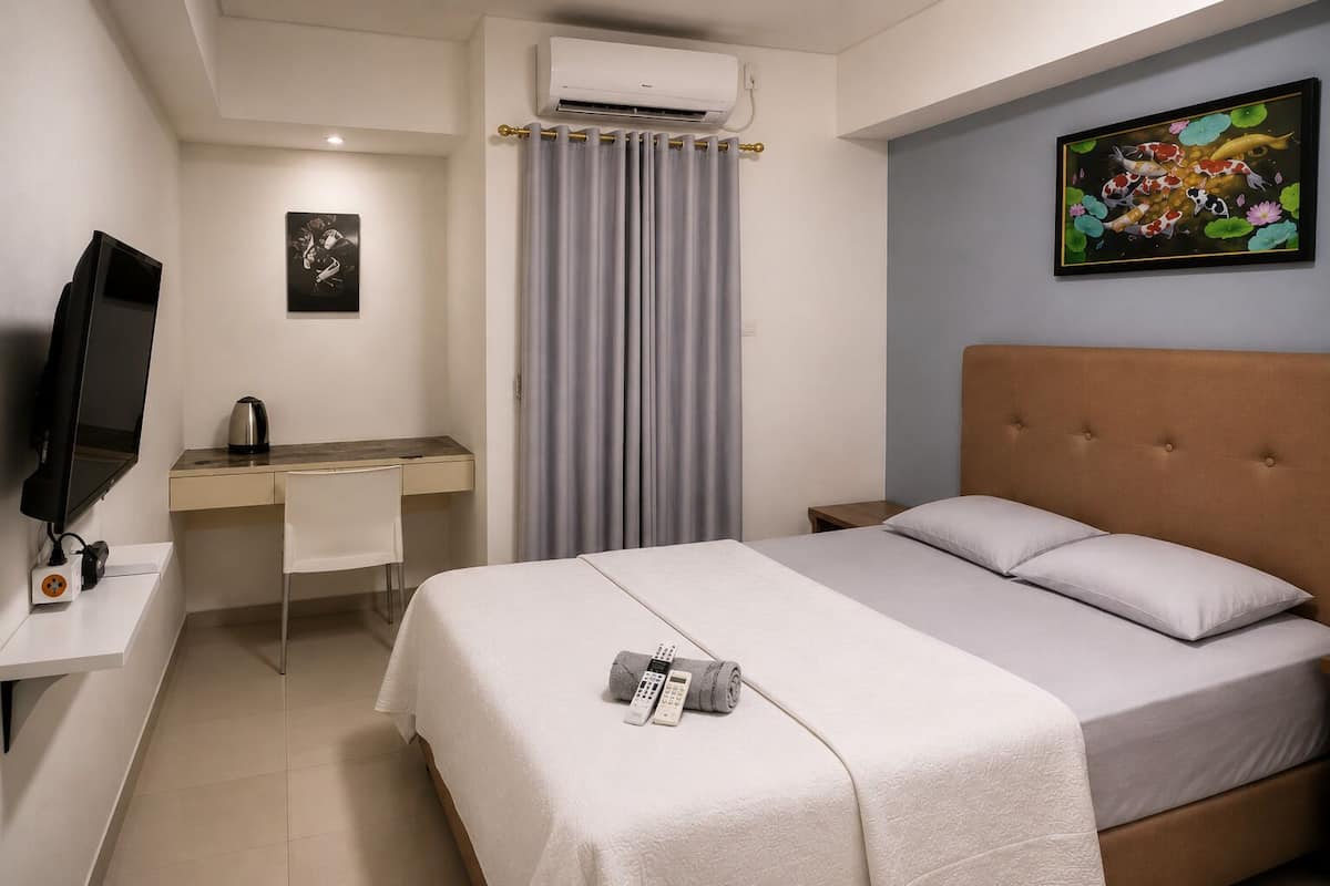 Una habitación de hotel con cama, escritorio con silla, televisión, aire acondicionado y un cuadro en la pared.