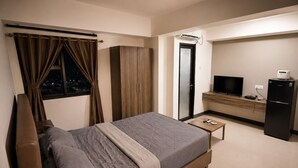 A modern hotel room with a bed, a TV, a refrigerator, and a desk. - 19 AVENUE Meeran By Reccoma (Tangerang)