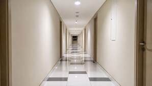 A long, narrow hotel corridor with a checkered floor pattern, doors on both sides, and recessed lighting on the ceiling. - 19 AVENUE Meeran By Reccoma (Tangerang)