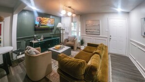 Uma sala de estar com sofá, mesa de centro, televisão e uma área de refeições com mesa e cadeiras.