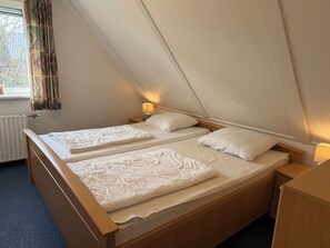 Ein Einzelbett mit Holzrahmen, ein Nachttisch mit Lampe und ein Fenster mit Vorhängen.