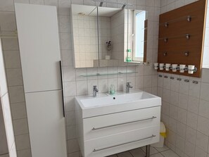 Ein modernes Badezimmer mit einem weißen Waschbecken, Spiegel und Schränken.