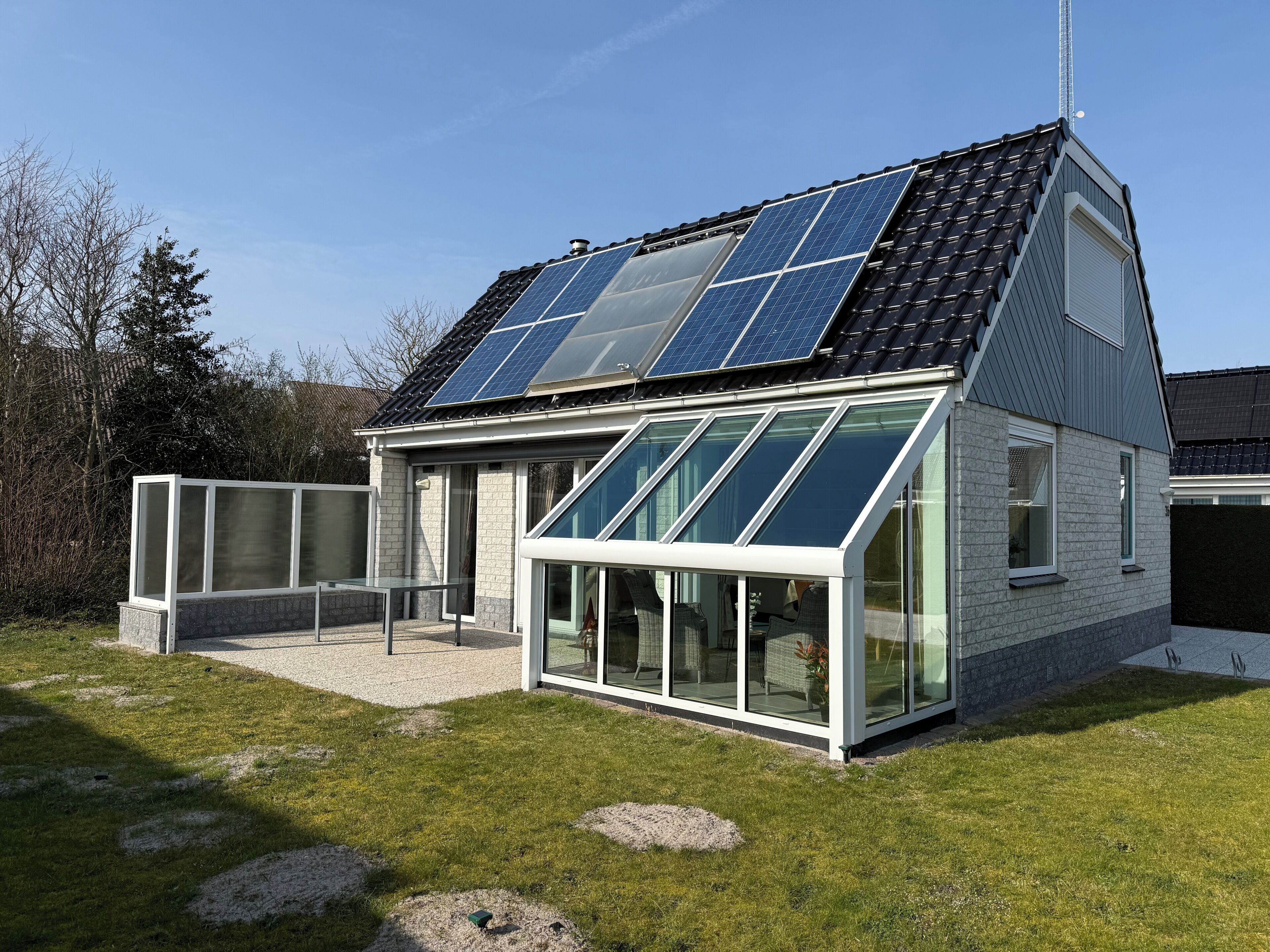 Ein modernes Haus mit Satteldach, Solaranlage, großen Glasfenstern und einer kleinen Terrasse.