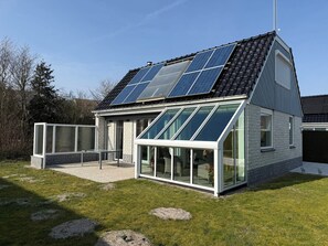 A modern house with a sloped roof, solar panels, large glass windows, and a small patio area. - Holiday home Bohemien in Sint Maartenszee in Callantsoog. Suitable for 6 people with 3 bedrooms. (Sint Maartensvlotbrug)
