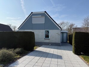 A modern building with a sloped roof, a large garage door, and a paved driveway. - Holiday home Bohemien in Sint Maartenszee in Callantsoog. Suitable for 6 people with 3 bedrooms. (Sint Maartensvlotbrug)
