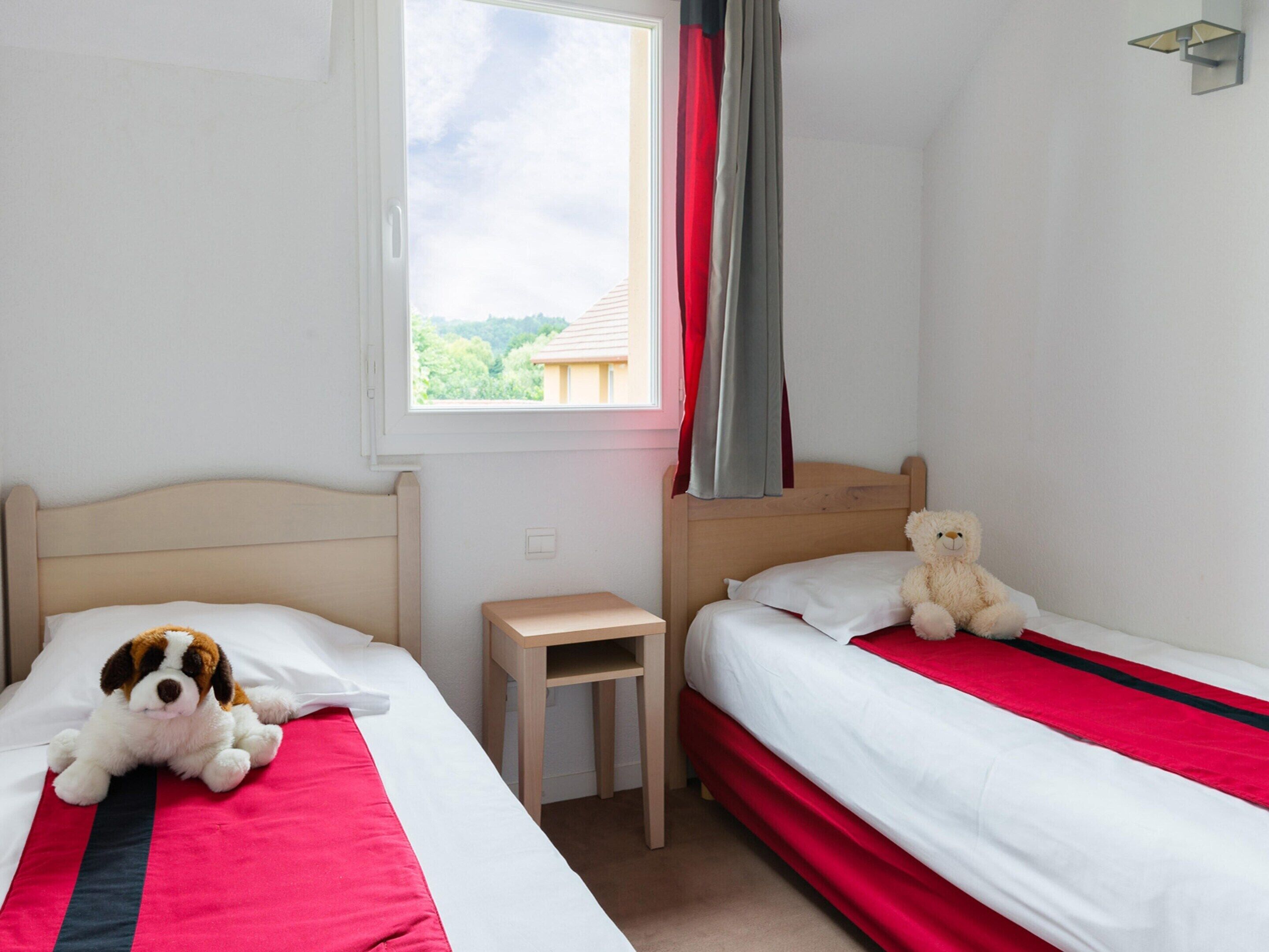Une chambre avec deux lits, une petite table et une fenêtre avec des rideaux.
