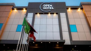 Fachada de hotel con un llamativo letrero que dice 'OPEN HOTEL', un asta con banderas y un diseño arquitectónico moderno.